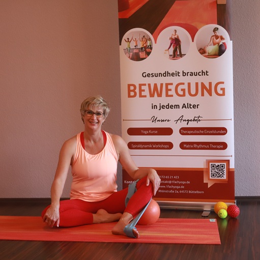 1fach Yoga | 1fach Gesund - Silke Wagner mit Teraband vor Plakat Gesundheit braucht Bewegung.